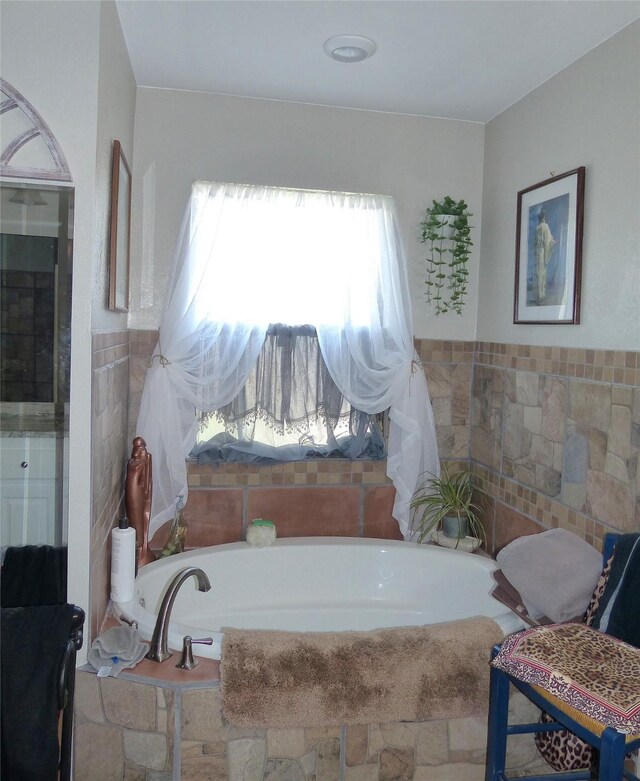 full bath with tile walls, a garden tub, and a wainscoted wall