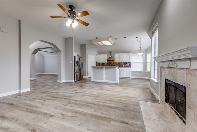 unfurnished living room featuring arched walkways, ceiling fan, light wood-style flooring, and a tile fireplace