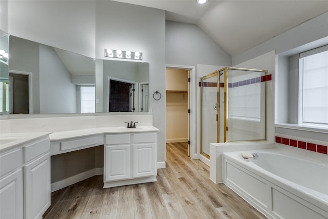 full bathroom featuring vanity, wood finished floors, lofted ceiling, a walk in closet, and a shower stall