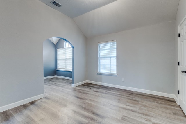 spare room with visible vents, baseboards, arched walkways, light wood finished floors, and vaulted ceiling