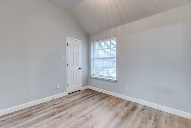 empty room featuring baseboards, light wood-style flooring, and vaulted ceiling