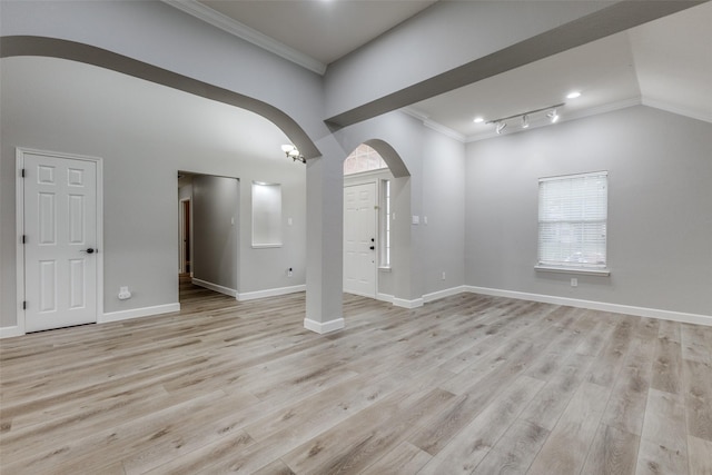 unfurnished living room with crown molding, arched walkways, vaulted ceiling, light wood-type flooring, and baseboards