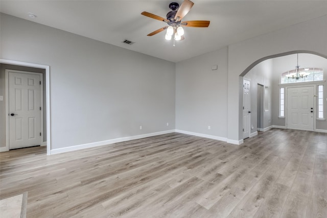 interior space featuring visible vents, arched walkways, light wood-style flooring, and ceiling fan with notable chandelier