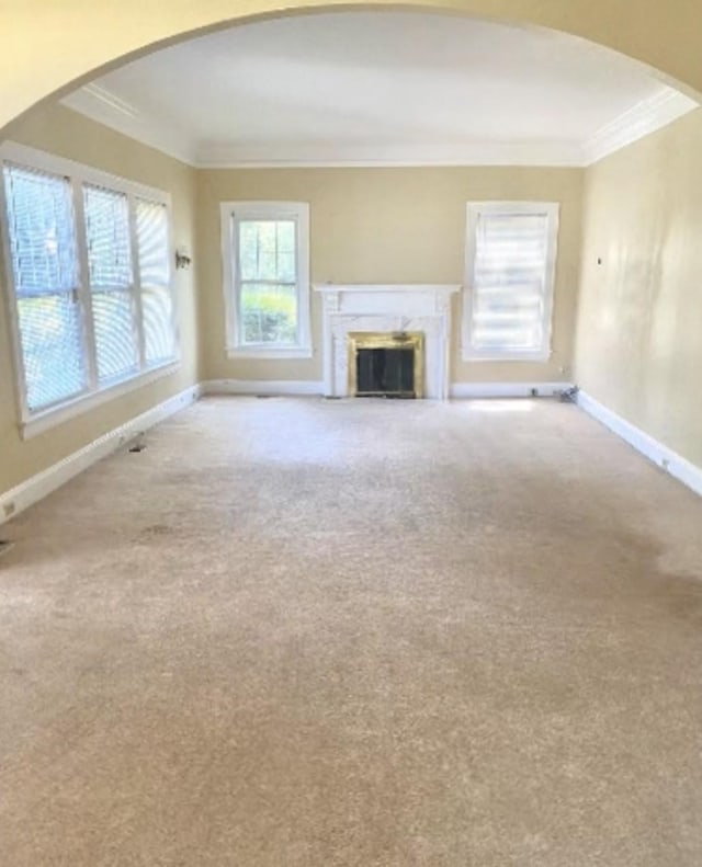 unfurnished living room with crown molding, a fireplace, arched walkways, carpet, and baseboards