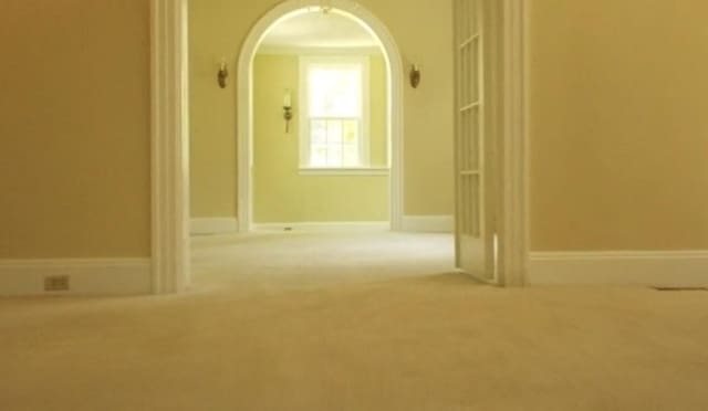 hallway with arched walkways, baseboards, and carpet floors