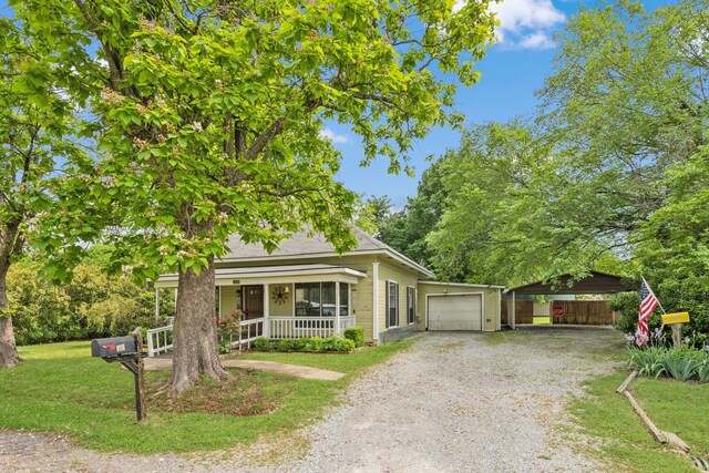 view of front facade featuring covered porch, a carport, gravel driveway, fence, and a front lawn