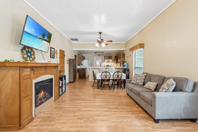 living area with visible vents, a ceiling fan, light wood-style floors, and a glass covered fireplace