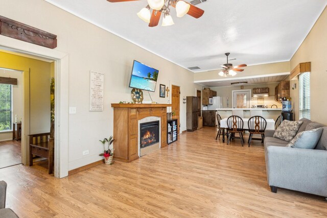 living room featuring a ceiling fan, a glass covered fireplace, visible vents, and light wood-style floors