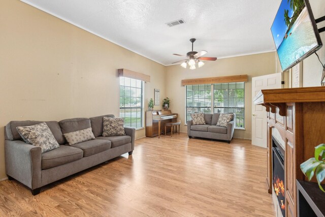 living area with light wood-style floors, crown molding, ceiling fan, and visible vents