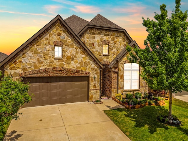 french provincial home with a shingled roof, stone siding, a garage, a yard, and driveway