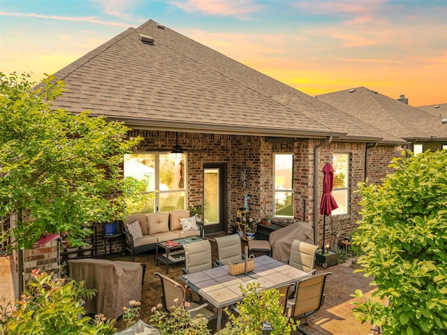 back of property with brick siding, an outdoor living space, a shingled roof, and a patio area