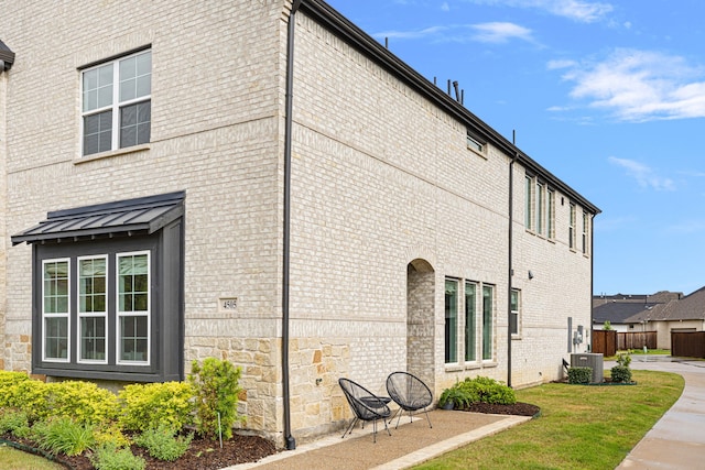 view of property exterior featuring fence, central AC unit, a lawn, and brick siding