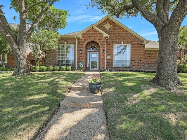 view of front facade featuring a shingled roof, a front lawn, and brick siding