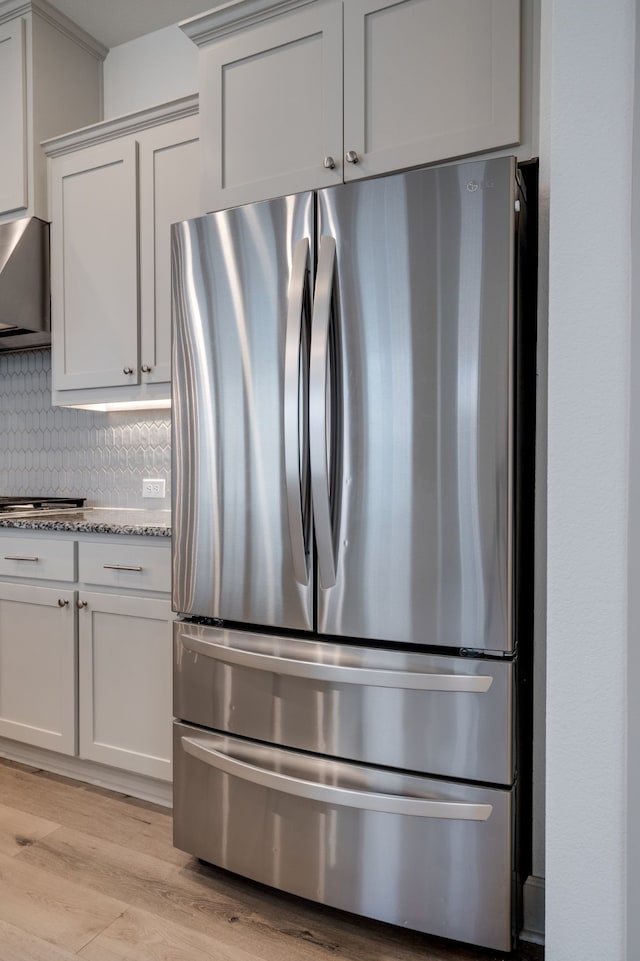 4402 Cypress Thorn Dr, Arlington, TX 76005 - kitchen featuring appliances with stainless steel finishes, tasteful backsplash, light stone countertops, light wood-type flooring, and wall chimney exhaust hood