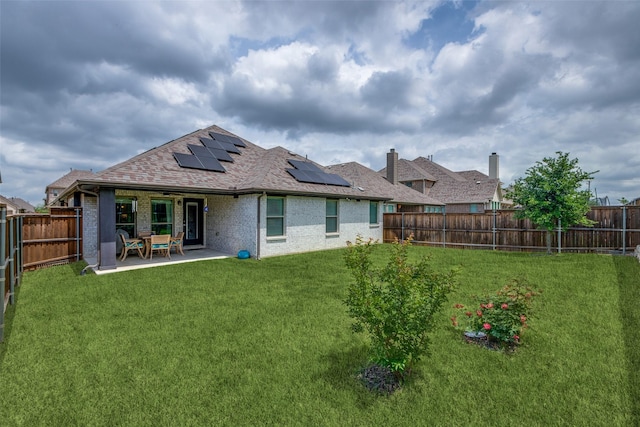 back of house with a fenced backyard, a lawn, solar panels, and brick siding