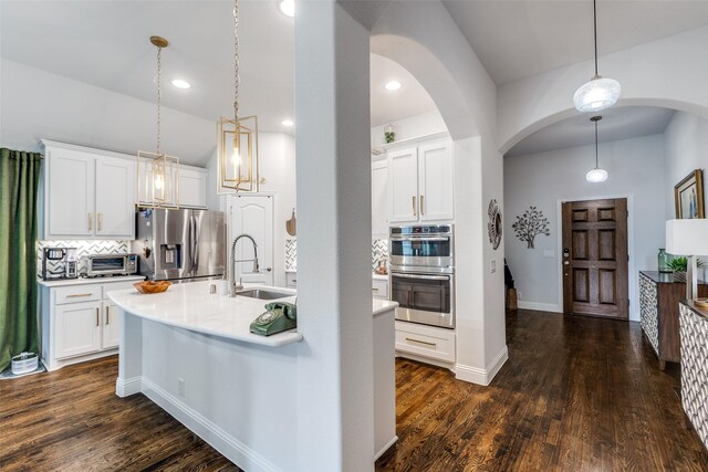 kitchen with decorative backsplash, appliances with stainless steel finishes, arched walkways, a sink, and light countertops