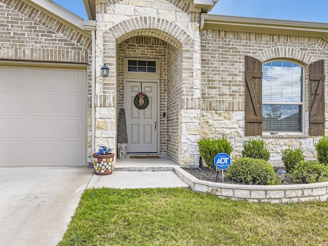 property entrance featuring an attached garage, driveway, brick siding, and stone siding
