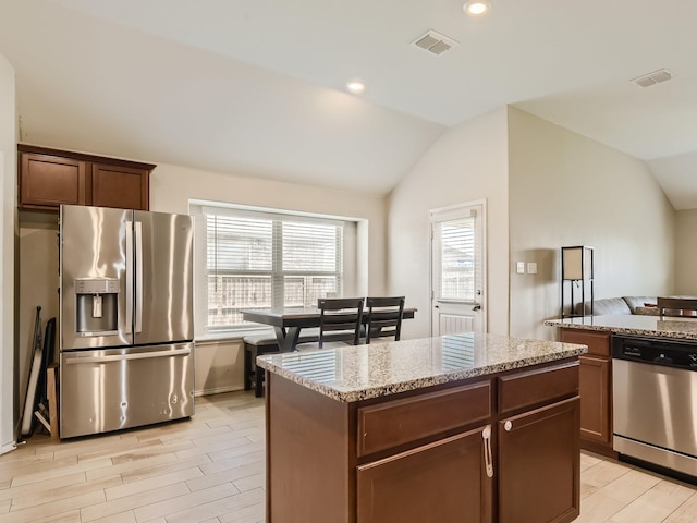 kitchen featuring vaulted ceiling, light stone counters, stainless steel appliances, and light wood finished floors