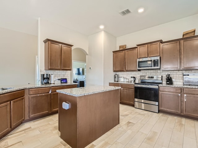 kitchen featuring light stone countertops, a center island, arched walkways, appliances with stainless steel finishes, and backsplash