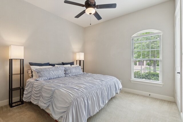 bedroom with baseboards, multiple windows, light carpet, and a ceiling fan
