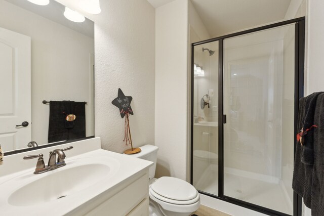 bathroom with vanity, toilet, a textured wall, and a stall shower