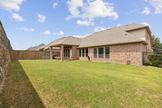 rear view of property featuring a yard, brick siding, a fenced backyard, and roof with shingles