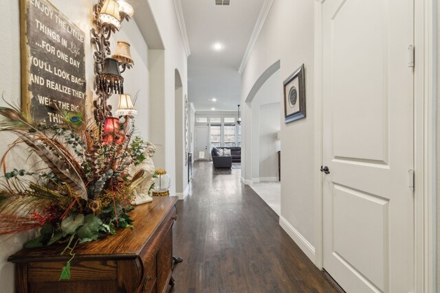 corridor featuring arched walkways, baseboards, wood finished floors, visible vents, and ornamental molding