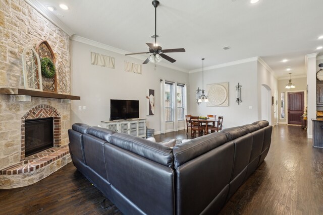 living area with crown molding, dark wood-style flooring, arched walkways, a large fireplace, and ceiling fan with notable chandelier