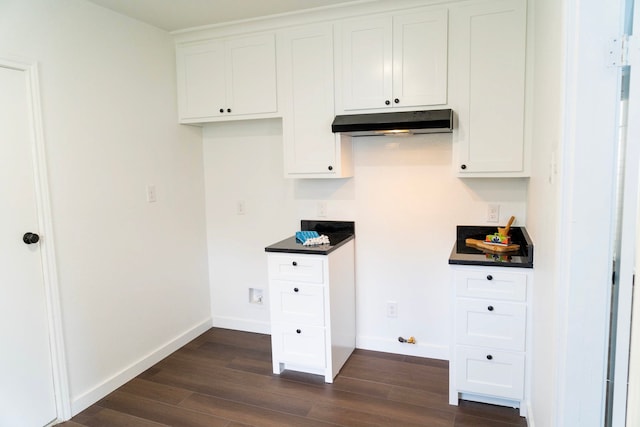 kitchen with baseboards, dark wood finished floors, under cabinet range hood, and dark countertops