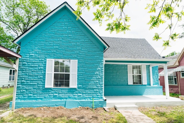 bungalow featuring covered porch, a shingled roof, and brick siding