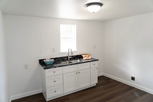 kitchen with a sink, dark stone counters, dark wood finished floors, and white cabinetry