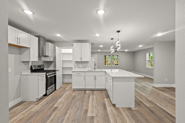 kitchen featuring a peninsula, light wood-style floors, stainless steel gas range, wall chimney exhaust hood, and a sink