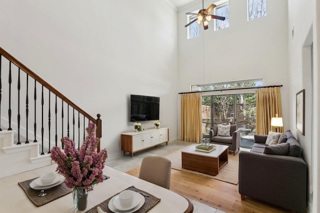 living room featuring light wood-style floors, a ceiling fan, stairs, and a towering ceiling