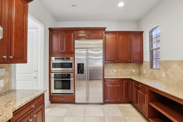 kitchen with tasteful backsplash, light stone countertops, dark brown cabinets, light tile patterned floors, and stainless steel appliances