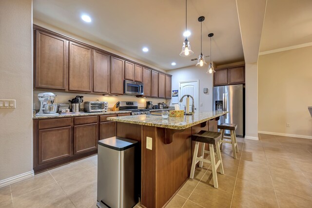 kitchen with a toaster, appliances with stainless steel finishes, light tile patterned floors, and a kitchen island with sink
