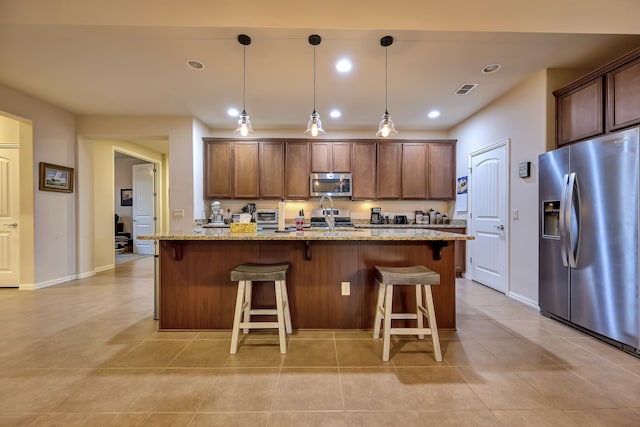 12521 Gritstone Dr, Denton, TX 76207 - kitchen with appliances with stainless steel finishes, a center island with sink, a breakfast bar area, light stone countertops, and light tile patterned flooring