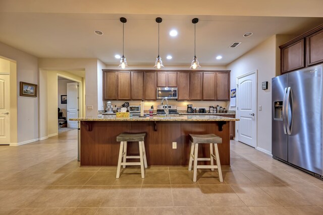 kitchen with visible vents, a kitchen island with sink, a kitchen breakfast bar, light stone counters, and stainless steel appliances
