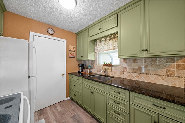 kitchen with freestanding refrigerator, green cabinetry, a sink, and light wood finished floors