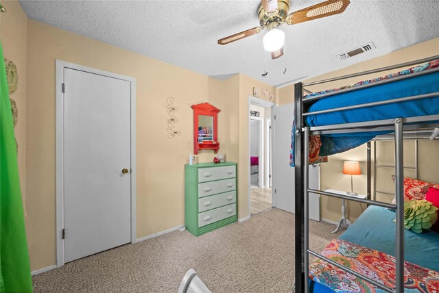 carpeted bedroom with visible vents, a textured ceiling, baseboards, and a ceiling fan