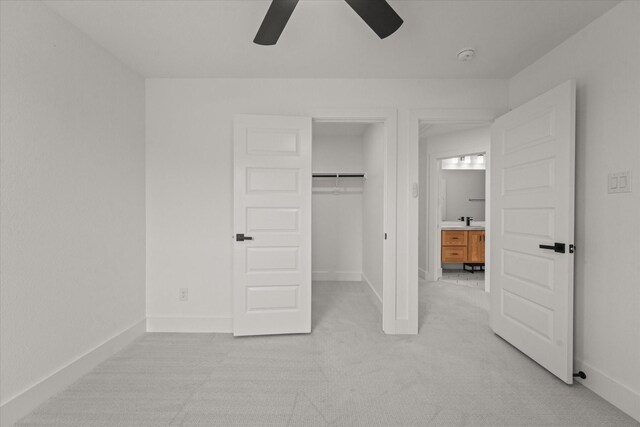 unfurnished bedroom featuring light colored carpet, a walk in closet, a ceiling fan, baseboards, and a closet