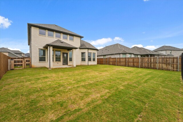 back of property with brick siding, a fenced backyard, and a yard