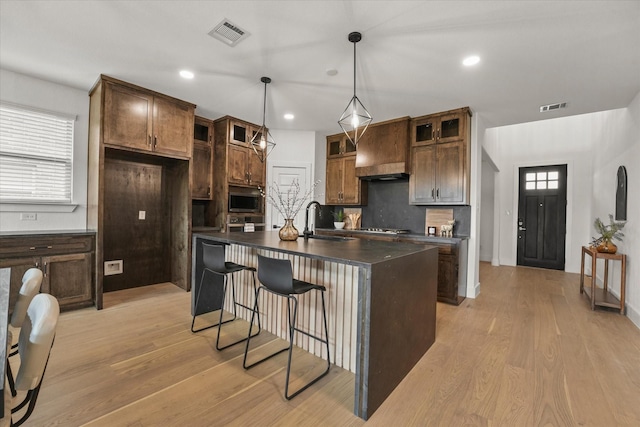 3805 Bluestem Blvd, Denton, TX 76226 - kitchen featuring custom range hood, dark countertops, stainless steel microwave, light wood finished floors, and recessed lighting