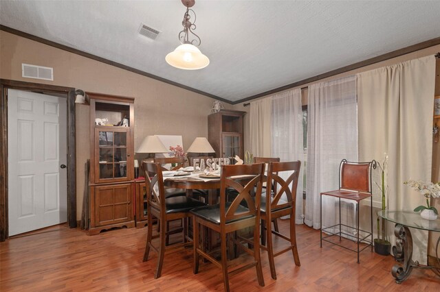 dining space featuring crown molding, vaulted ceiling, wood finished floors, and visible vents