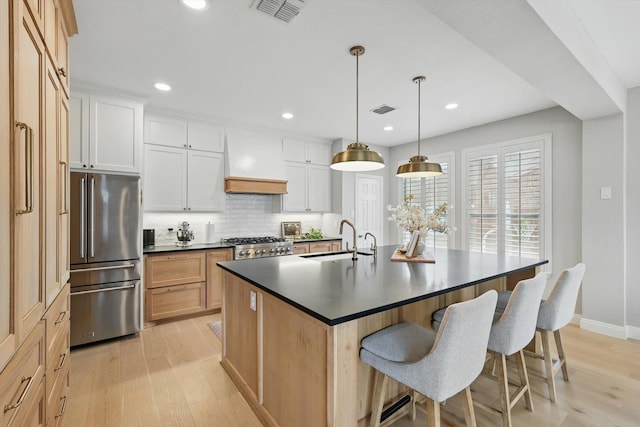 kitchen featuring high end fridge, dark countertops, a sink, premium range hood, and visible vents