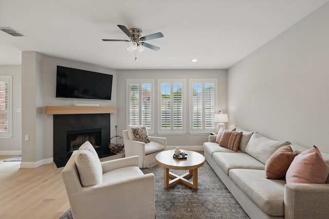 living area featuring ceiling fan, a fireplace, light wood-style floors, baseboards, and visible vents