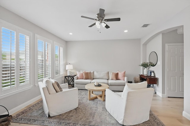 living area with light wood finished floors, arched walkways, a ceiling fan, baseboards, and visible vents