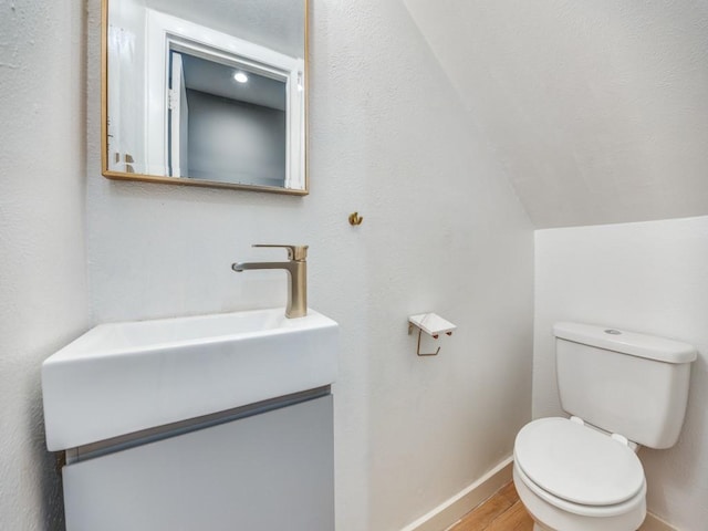 3817 Rawlins St Unit 103, Dallas, TX 75219 - bathroom with toilet, wood finished floors, lofted ceiling, baseboards, and vanity