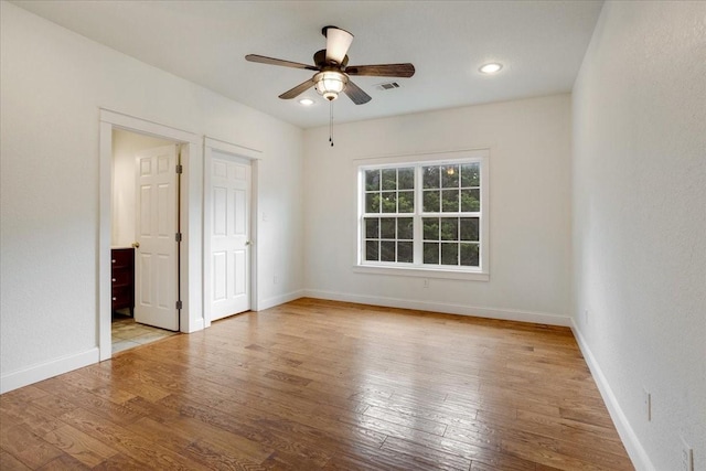 empty room featuring wood-type flooring, baseboards, ceiling fan, and visible vents