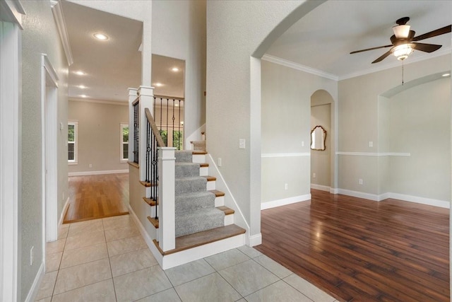 staircase featuring arched walkways, ceiling fan, ornamental molding, and wood finished floors