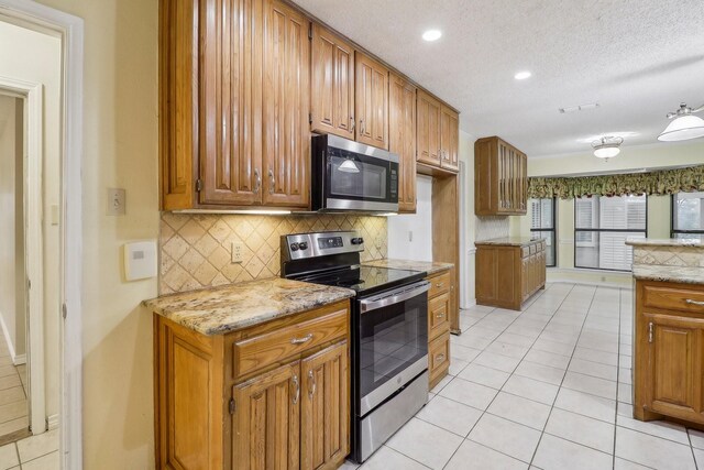 kitchen with decorative backsplash, light tile patterned floors, brown cabinets, and stainless steel appliances